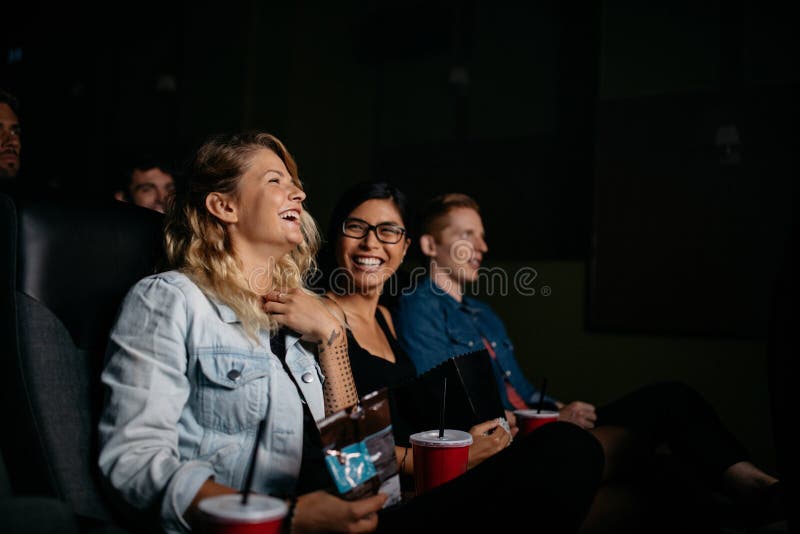 Group of young people watching movie in cinema. Friends sitting in movie theater with popcorn and drinks. Group of young people watching movie in cinema. Friends sitting in movie theater with popcorn and drinks.