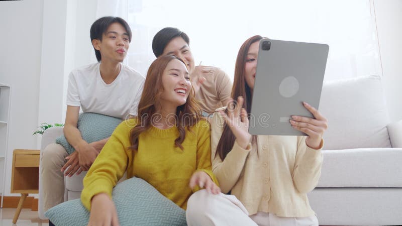 Groupe de jeunes amis asiatiques assis sur un canapé en prenant un selfie ou un appel vidéo en utilisant la tablette numérique dan banque de vidéos