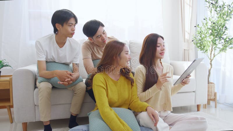 Groupe de jeunes amis asiatiques assis sur un canapé en prenant un selfie ou un appel vidéo en utilisant la tablette numérique dan banque de vidéos