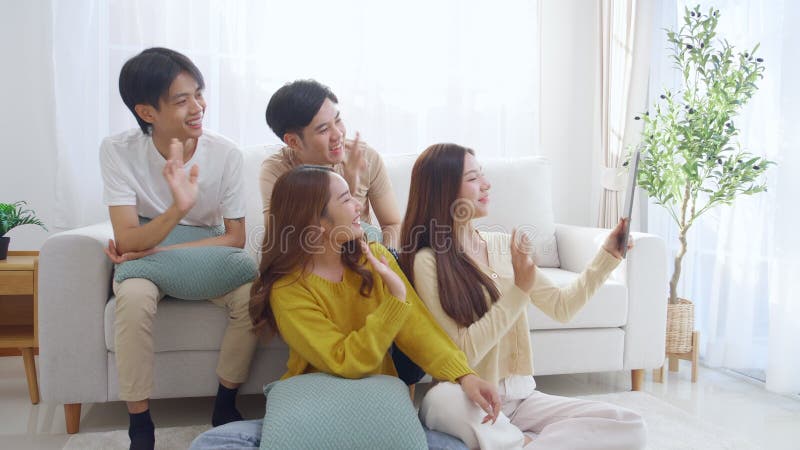 Groupe de jeunes amis asiatiques assis sur un canapé en prenant un selfie ou un appel vidéo en utilisant la tablette numérique dan banque de vidéos