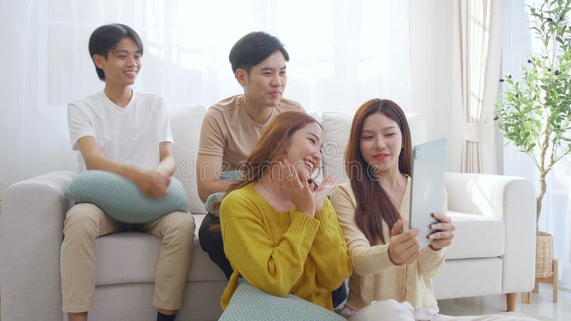 Groupe de jeunes amis asiatiques assis sur un canapé en prenant un selfie ou un appel vidéo en utilisant la tablette numérique dan banque de vidéos