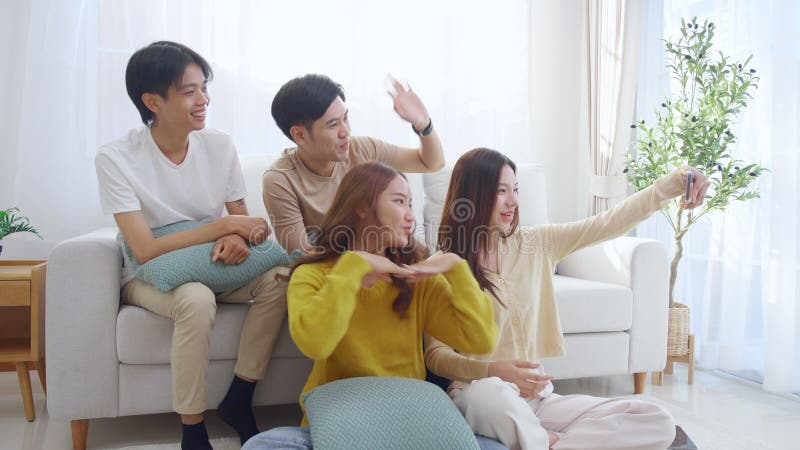 Groupe de jeunes amis asiatiques assis sur un canapé en prenant un selfie ou un appel vidéo en utilisant un téléphone intelligent clips vidéos