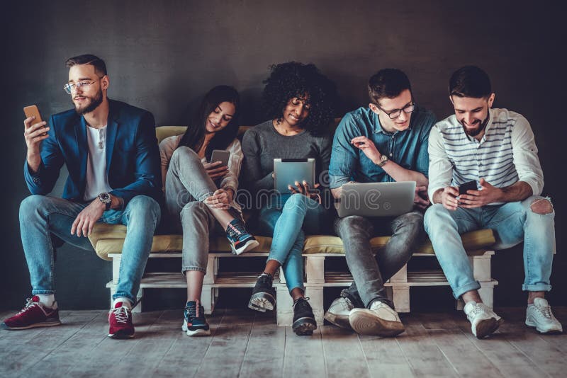 Groupe de jeunes heureux assis sur un canapé et utilisant une tablette numérique et un ordinateur portable photo stock