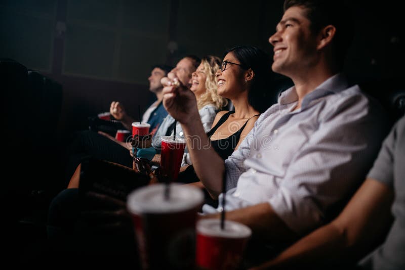 Group of people in theater with popcorn and drinks. Young friends watching movie in cinema. Group of people in theater with popcorn and drinks. Young friends watching movie in cinema.