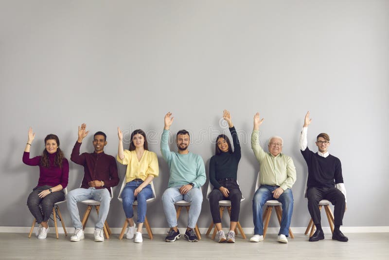 Group of happy smiling diverse people in casual clothes sitting on chairs in row and raising hands, unanimously supporting and voting for a suggested idea. Group of happy smiling diverse people in casual clothes sitting on chairs in row and raising hands, unanimously supporting and voting for a suggested idea