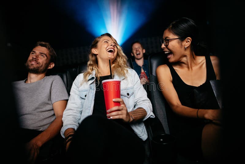 Young women with friends in cinema hall watching movie. Group of people watching movie in theater and laughing. Young women with friends in cinema hall watching movie. Group of people watching movie in theater and laughing.