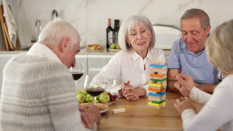 Groupe de quatre amis matures joue jeu de société avec des blocs en bois dans la cuisine banque de vidéos