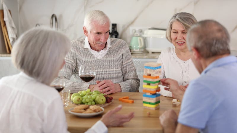 Groupe de quatre amis matures joue jeu de société avec des blocs en bois dans la cuisine banque de vidéos