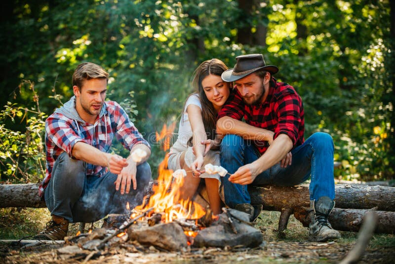 Group of backpackers relaxing near campfire. Friends spend leisure weekend forest nature background. Tourists relaxing. Happy young people camping in woods. Cheerful men and women making picnic. Group of backpackers relaxing near campfire. Friends spend leisure weekend forest nature background. Tourists relaxing. Happy young people camping in woods. Cheerful men and women making picnic