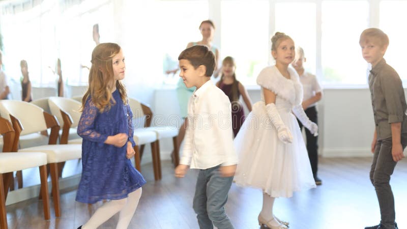 Groupe de tweets joyeux expressifs filles et garçons en mode formel danse torsion énergique dans la salle de classe éclairée banque de vidéos