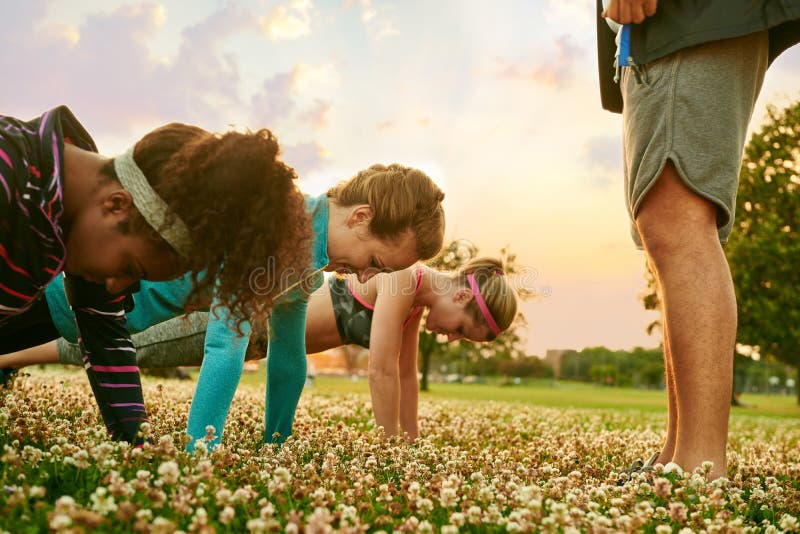 Groupe divers de femmes pendant une formation de forme physique faisant des pousées au coucher du soleil en parc naturel images libres de droits Groupe divers de femmes pendant une formation de forme physique faisant des pousées au coucher du soleil en parc naturel images libres de droits