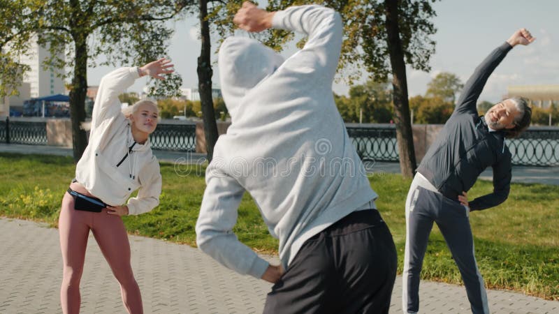 Groupe diversifié de personnes qui s'entraînent à l'extérieur en faisant du sport souriant dans un contexte urbain banque de vidéos