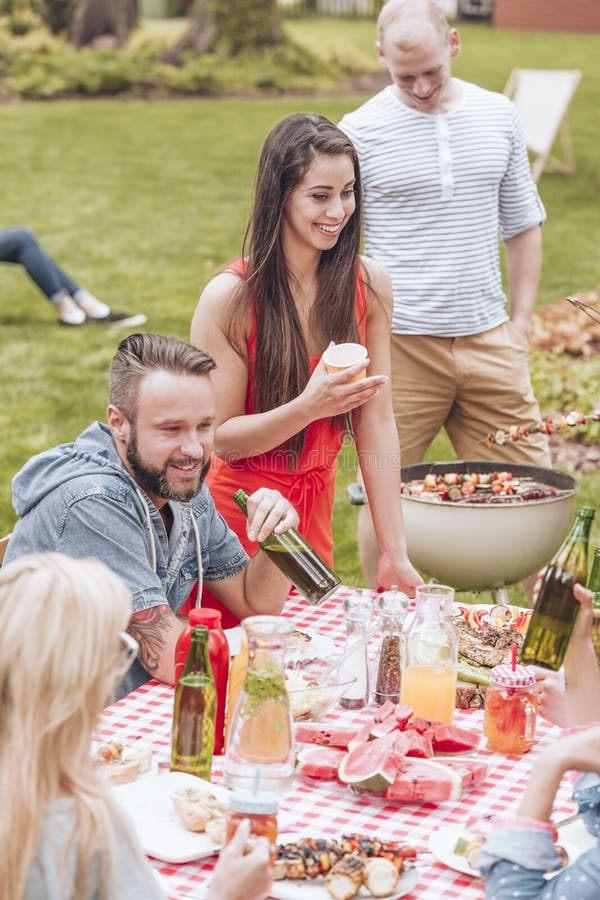 Groupe heureux d'amis ayant une partie de gril par une table complètement de f image stock Groupe heureux d'amis ayant une partie de gril par une table complètement de f image stock