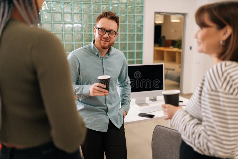 Happy group of ethnically diverse young men and women relaxing while having coffee break at work in light modern office room. Relaxed coworkers enjoying coffee break and chatting at workplace. Happy group of ethnically diverse young men and women relaxing while having coffee break at work in light modern office room. Relaxed coworkers enjoying coffee break and chatting at workplace.