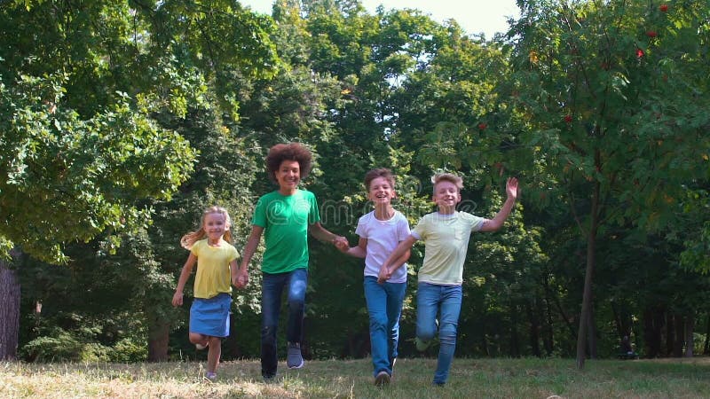 Groupe multiracial d'amis qui courent la main dans l'herbe, relations amicales, amusement