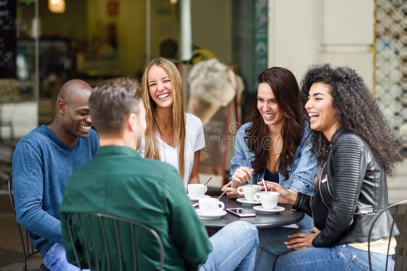 Multiracial group of five friends having a coffee together. Three women and two men at cafe, talking, laughing and enjoying their time. Lifestyle and friendship concepts with real people models. Multiracial group of five friends having a coffee together. Three women and two men at cafe, talking, laughing and enjoying their time. Lifestyle and friendship concepts with real people models