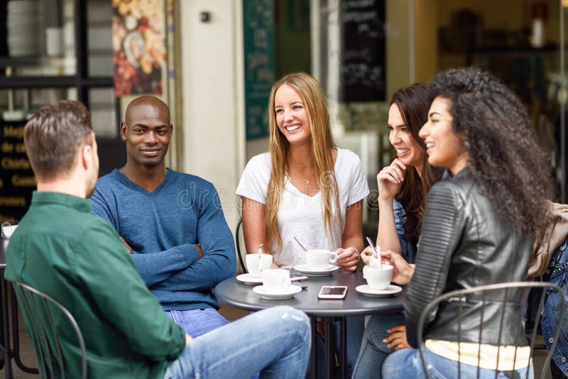 Multiracial group of five friends having a coffee together. Three women and two men at cafe, talking, laughing and enjoying their time. Lifestyle and friendship concepts with real people models. Multiracial group of five friends having a coffee together. Three women and two men at cafe, talking, laughing and enjoying their time. Lifestyle and friendship concepts with real people models