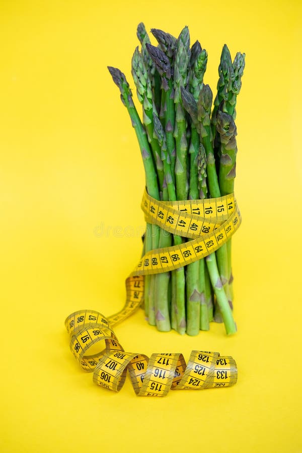 Groupe vert frais d'asperge avec la bande de mesure d'isolement au-dessus du fond jaune photographie stock Groupe vert frais d'asperge avec la bande de mesure d'isolement au-dessus du fond jaune photographie stock