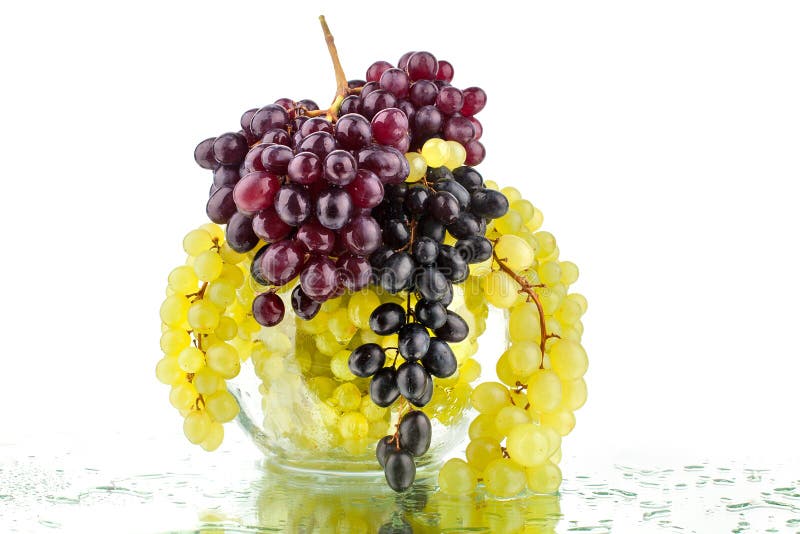 Groupes de raisins rouges et blancs dans le vase rond en verre sur le fond blanc de miroir avec des baisses de réflexion et d'eau photographie stock libre de droits Groupes de raisins rouges et blancs dans le vase rond en verre sur le fond blanc de miroir avec des baisses de réflexion et d'eau photographie stock libre de droits