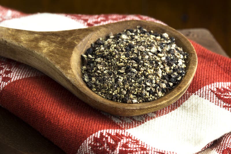 Coarse ground pepper in wooden spoon on red and white napkin. Coarse ground pepper in wooden spoon on red and white napkin