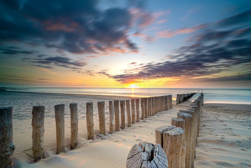 Groynes and wave breakers in a smooth sea just before sunset at a Dutch coast