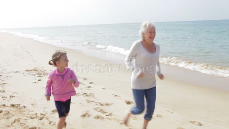 Großmutter und Enkelin, die zusammen entlang Strand laufen