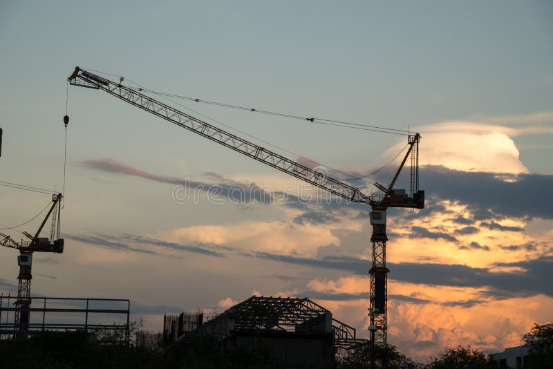 Gru di costruzione e siluette industriali della costruzione sopra il sole fotografia stock Gru di costruzione e siluette industriali della costruzione sopra il sole fotografia stock