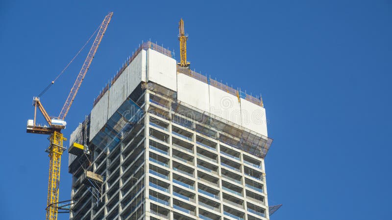 Crane and building construction site against blue sky with blank white billboard for advertisement at the top of tower architecture. Crane and building construction site against blue sky with blank white billboard for advertisement at the top of tower architecture.