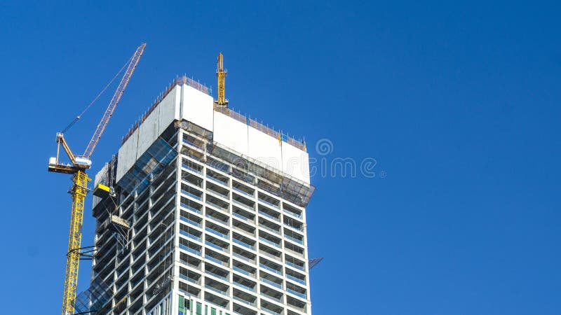 Crane and building construction site against blue sky with blank white billboard for advertisement at the top of tower architecture. Crane and building construction site against blue sky with blank white billboard for advertisement at the top of tower architecture.