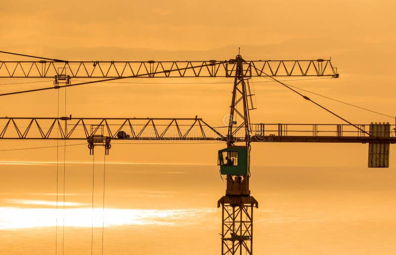 Gru a torre della costruzione contro l'oceano ad alba immagine stock libera da diritti Gru a torre della costruzione contro l'oceano ad alba immagine stock libera da diritti