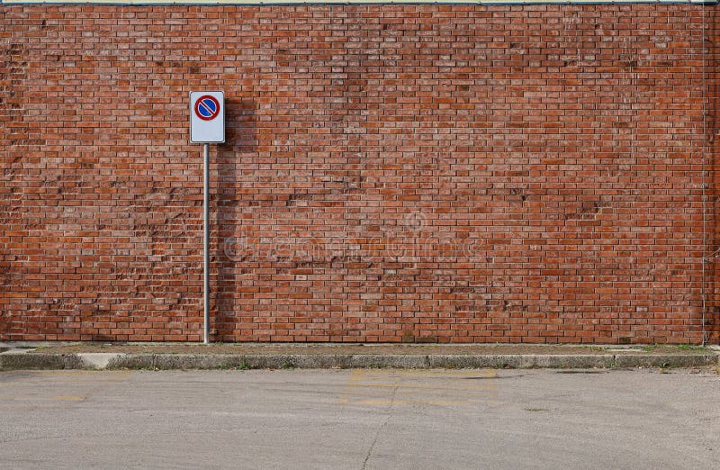 Grunge brick wall with a no stop road sign. A sidewalk and asphalt road in front.