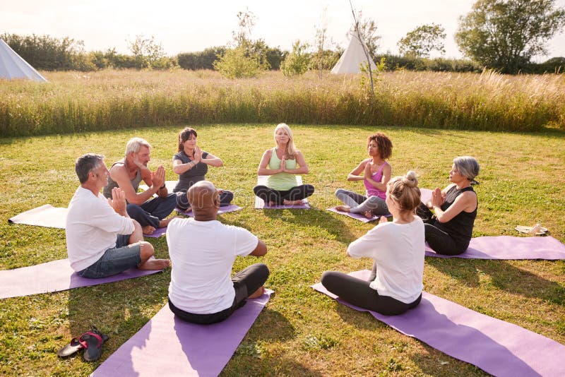 Group Of Mature Men And Women In Class At Outdoor Yoga Retreat Sitting Circle Meditating. Group Of Mature Men And Women In Class At Outdoor Yoga Retreat Sitting Circle Meditating
