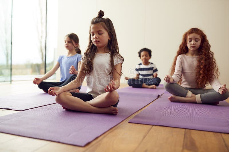 Group Of Children Sitting On Exercise Mats And Meditating In Yoga Studio. Group Of Children Sitting On Exercise Mats And Meditating In Yoga Studio