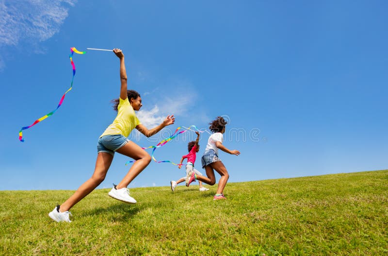 Profile view of a group of running girls waving with ribbon in park over blue sky. Profile view of a group of running girls waving with ribbon in park over blue sky