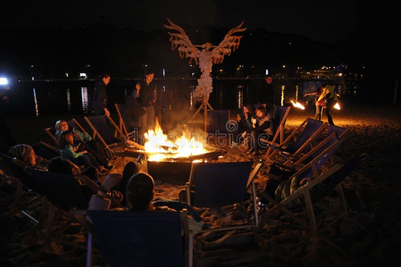 Grupa młodych zwolenników ukraińskiego pogańskiego kultu siedzącego wokół ognia na piaszczystej plaży rzeki
