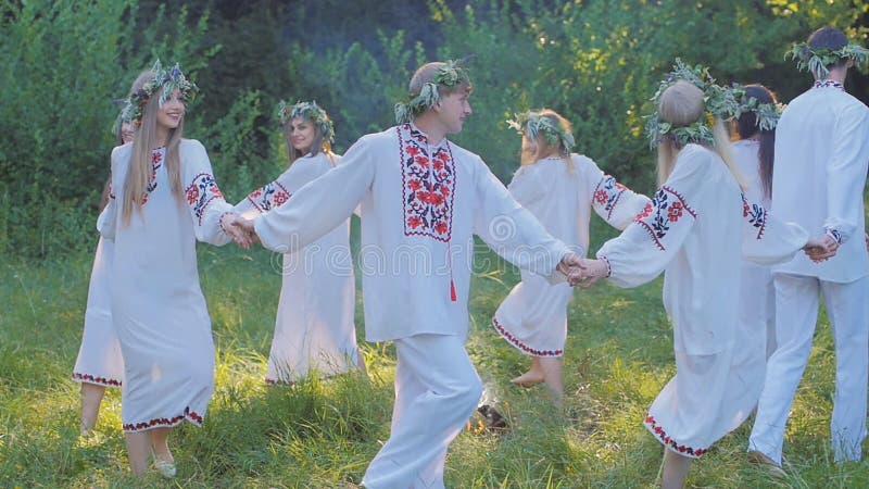 Grupa młodzi ludzie w krajowych Slawistycznych kostiumach tanczy w okręgu wokoło ogienia Krajowi Slawistyczni obrządki i tanowie
