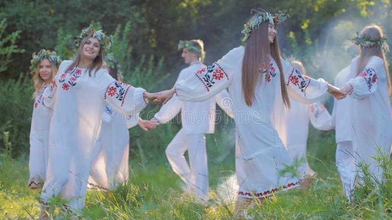 Grupa młodzi ludzie w krajowych Slawistycznych kostiumach tanczy w okręgu wokoło ogienia Krajowi Slawistyczni obrządki i tanowie