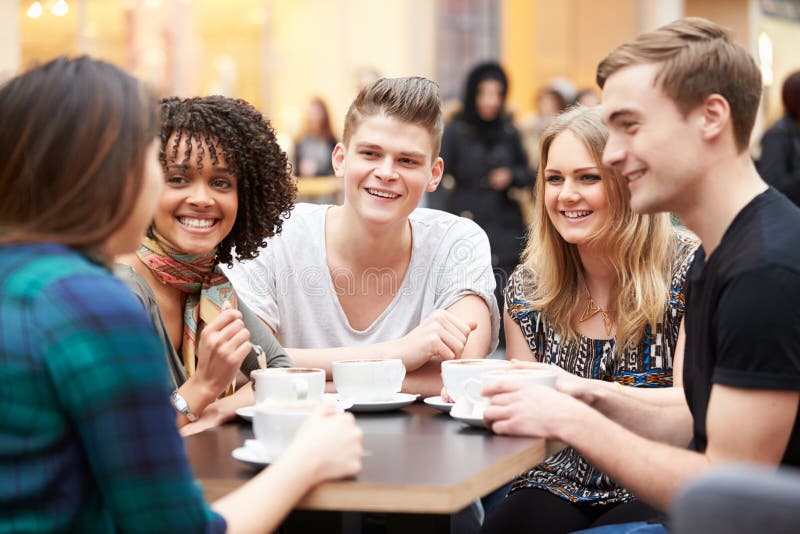 Group Of Young Friends Meeting In Cafe Sitting At Table Chatting. Group Of Young Friends Meeting In Cafe Sitting At Table Chatting