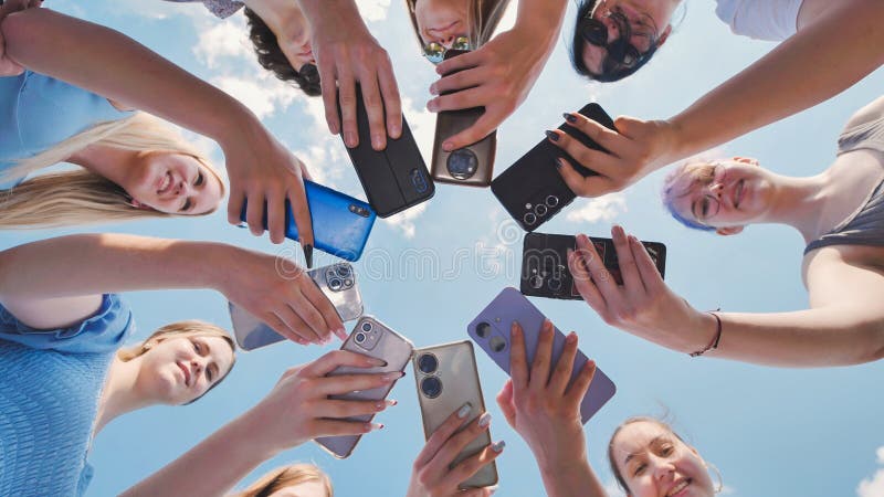 Grupa nastolatków i chłopców trzymających smartfony tworzące okrąg z telefonami komórkowymi przeciwko niebieskiemu niebu. fotografia royalty free