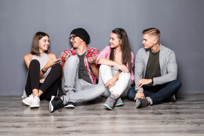 Grupa piękni ucznie w przypadkowych ubraniach używać gadżet, opowiadający i ono uśmiecha się, podczas gdy siedzący wpólnie na pod obrazy royalty free Grupa piękni ucznie w przypadkowych ubraniach używać gadżet, opowiadający i ono uśmiecha się, podczas gdy siedzący wpólnie na pod obrazy royalty free