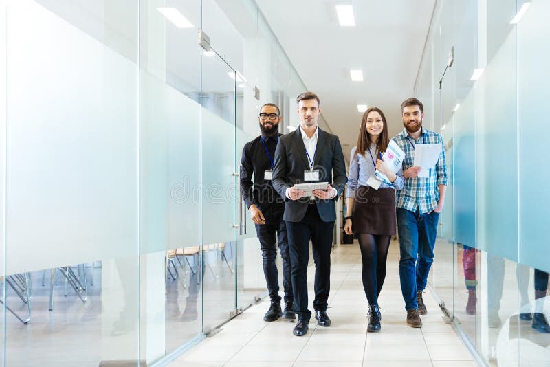 Full length of group of happy young business people walking the corridor in office together. Full length of group of happy young business people walking the corridor in office together