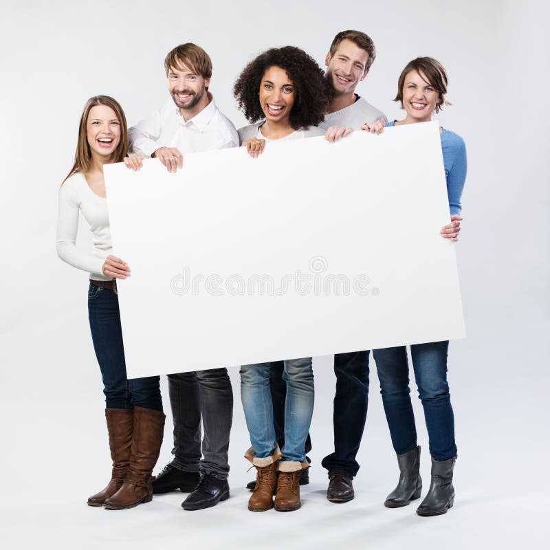 Group of diverse multiethnic happy young people posing with a blank white rectabgular sign with copyspace for your advertisement or text on a grey background. Group of diverse multiethnic happy young people posing with a blank white rectabgular sign with copyspace for your advertisement or text on a grey background
