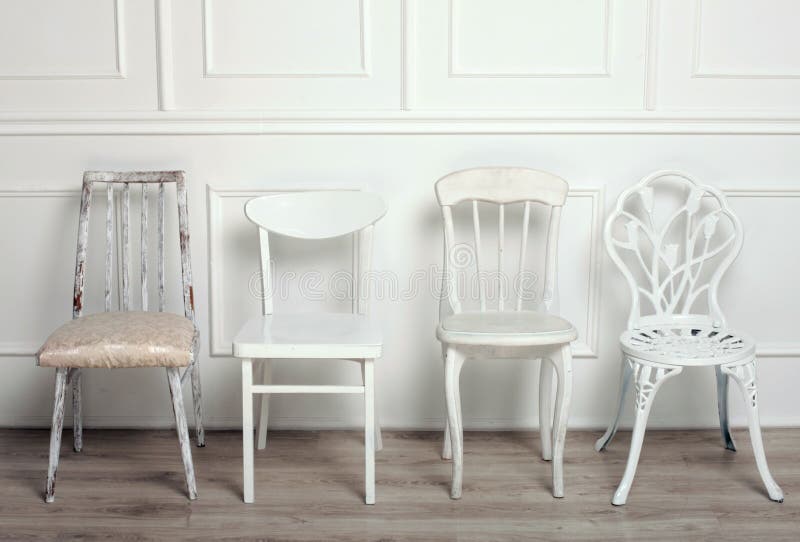 Set of white wooden vintage chairs standing in front of a white wooden wall on light parquet floor. Set of white wooden vintage chairs standing in front of a white wooden wall on light parquet floor.