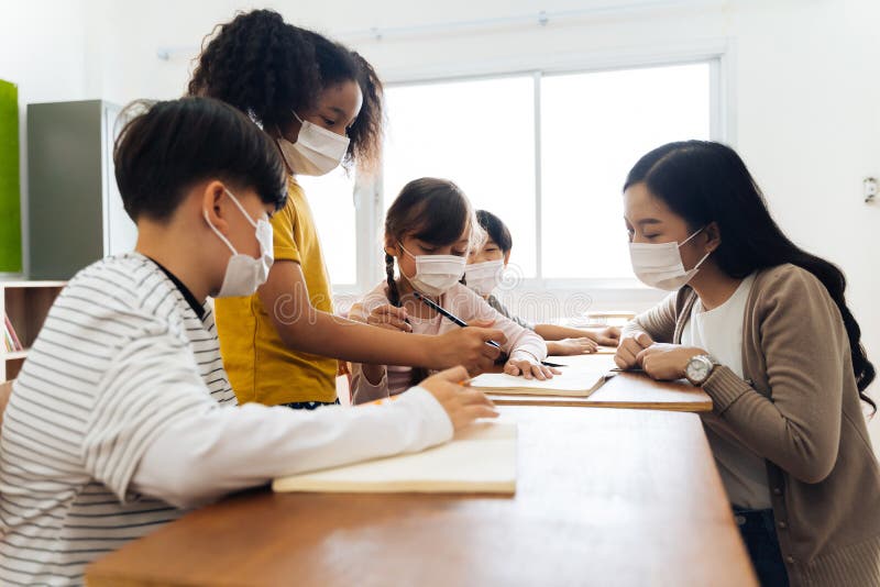 Group of diverse students in school building discussing in group study class. Elementary pupils are wearing a face mask while brainstorming. Covid-19 school reopen concept. Group of diverse students in school building discussing in group study class. Elementary pupils are wearing a face mask while brainstorming. Covid-19 school reopen concept