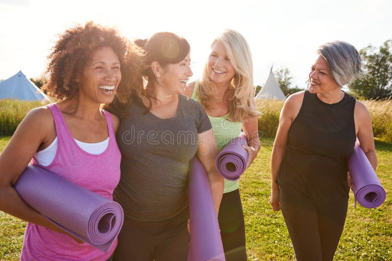 Group Of Mature Female Friends On Outdoor Yoga Retreat Walking Along Path Through Campsite. Group Of Mature Female Friends On Outdoor Yoga Retreat Walking Along Path Through Campsite