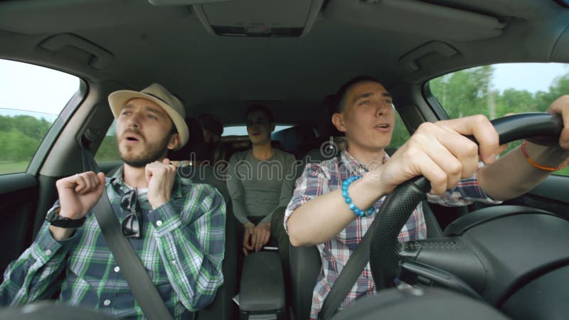 Grupo de amigos felices en coche que cantan y que bailan mientras que viaje por carretera de la impulsión