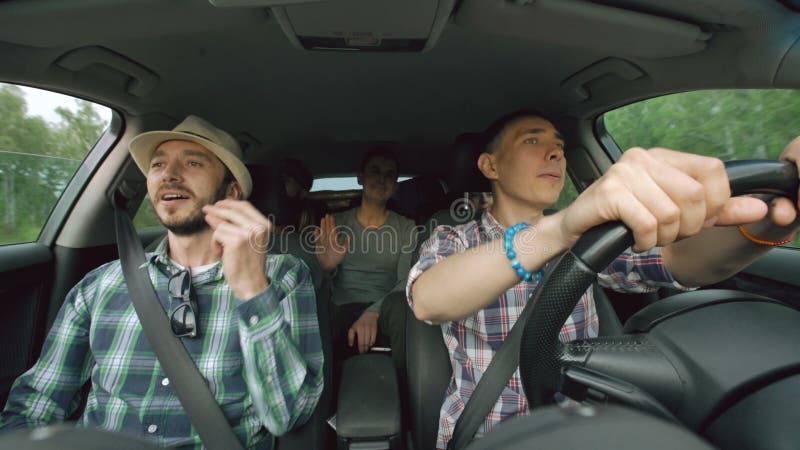 Grupo de amigos felices en coche que cantan y que bailan mientras que viaje por carretera de la impulsión