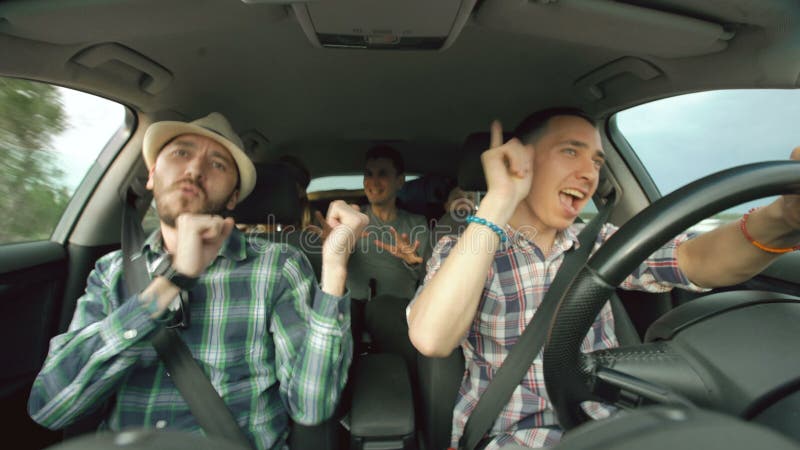 Grupo de amigos felices en coche que cantan y que bailan mientras que viaje por carretera de la impulsión