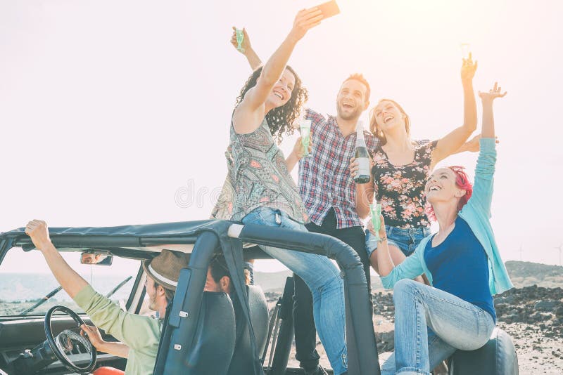 Group of happy friends making party on a jeep car - Young people having fun drinking champagne and taking photo selfie during their road trip - Friendship, party, youth addiction lifestyle concept. Group of happy friends making party on a jeep car - Young people having fun drinking champagne and taking photo selfie during their road trip - Friendship, party, youth addiction lifestyle concept