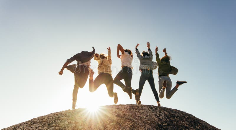 Rear view of group of happy friends having fun on mountain top. Men and women jumping on mountain top against sunset. Rear view of group of happy friends having fun on mountain top. Men and women jumping on mountain top against sunset.